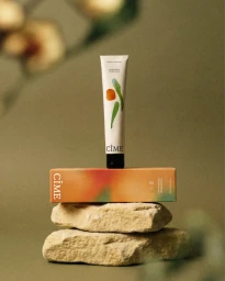 CIME skincare product tube standing upright on its packaging box, stacked on top of two natural stone blocks