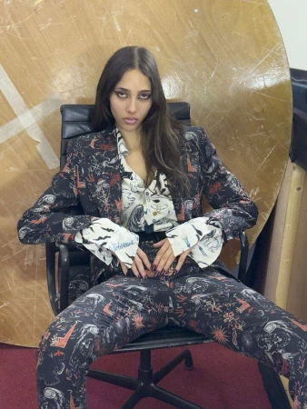 Model seated in an office chair wearing a patterned suit and printed shirt for Vivienne Westwood Fall 2025 campaign.
