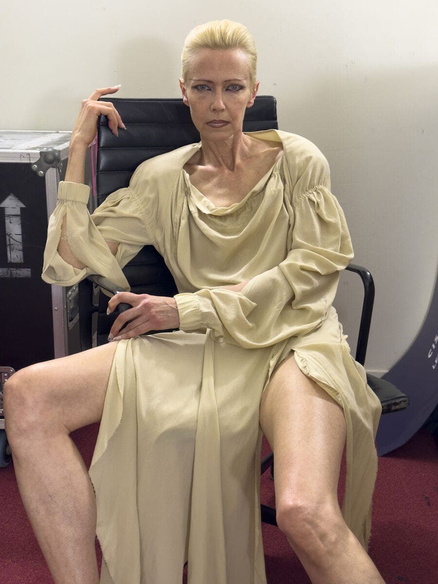Model with blonde hair wearing a loose cream dress sitting in a black office chair