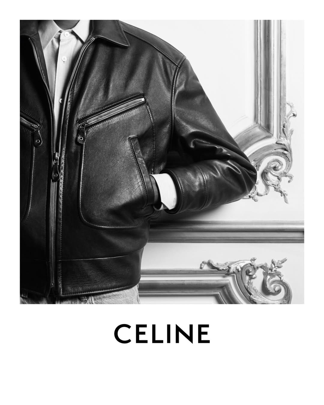 Close-up black and white image of a person wearing a leather jacket and button-up shirt leaning against an ornate wall panel.