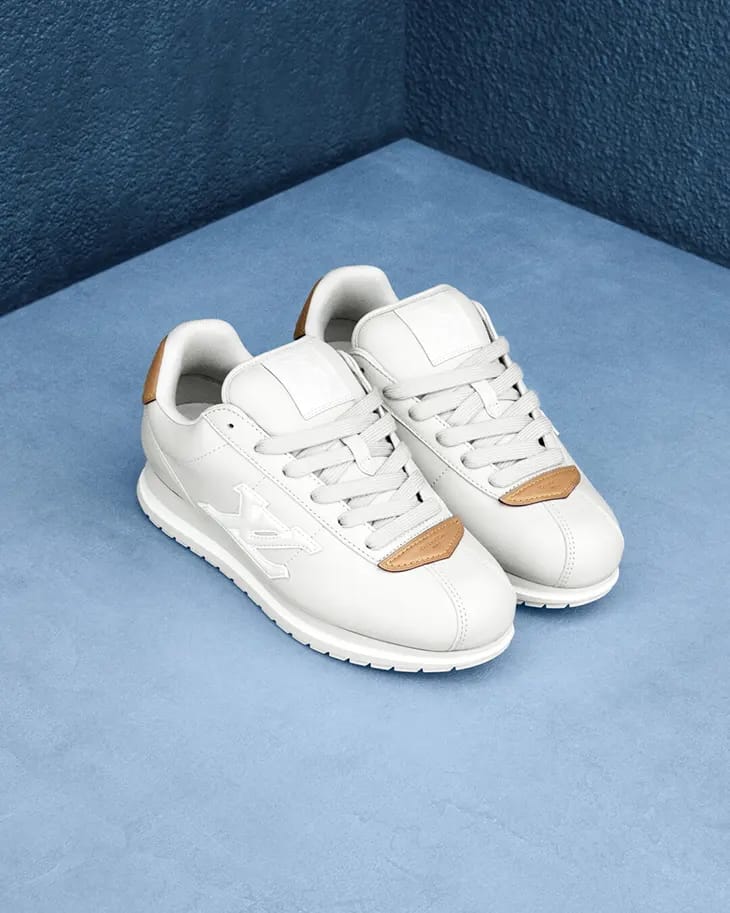 A pair of white leather sneakers with brown leather accents resting on a textured blue surface.