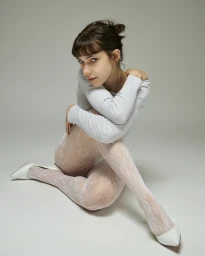Model Brookelle McKenzie seated in white lace tights and heels against a grey seamless backdrop for Mackenzie