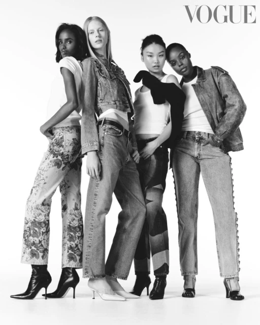 Four fashion models of diverse ethnicities pose in a black and white studio shot, wearing denim outfits and fashionable shoes against a white backdrop.