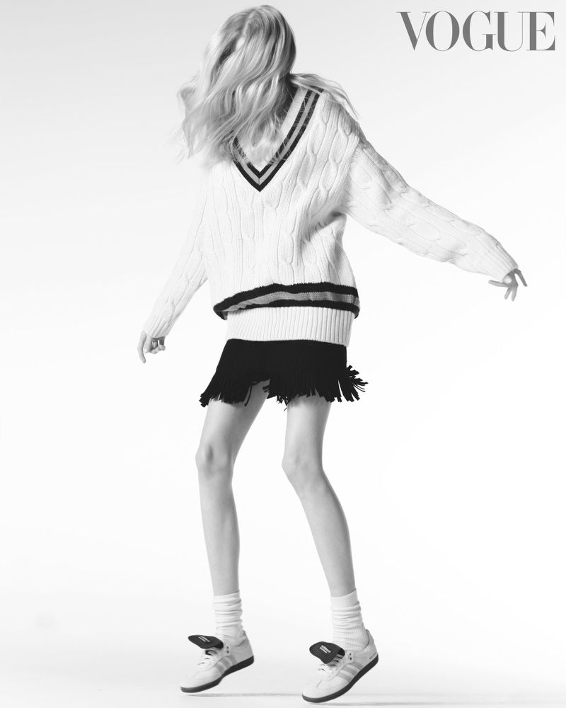Fashion shot: Woman in a white sweater and black skirt poses against a white background with the Vogue logo visible. Black and white.