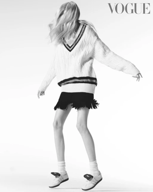 Fashion shot: Woman in a white sweater and black skirt poses against a white background with the Vogue logo visible. Black and white.