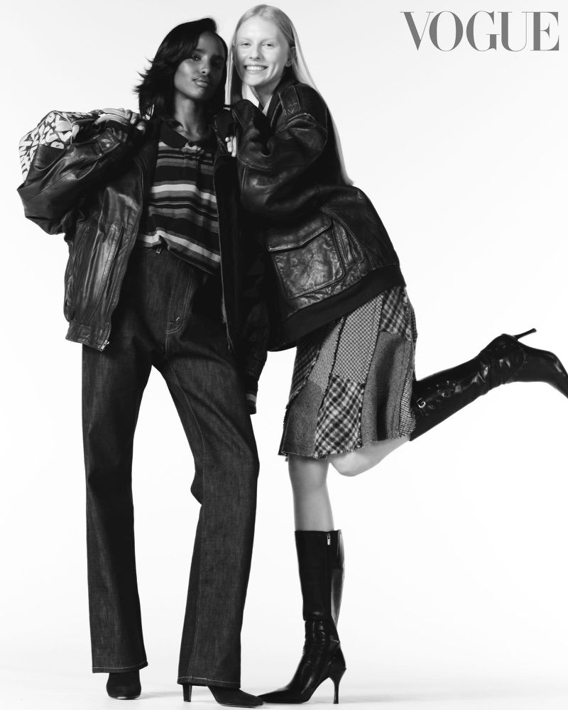 Two fashion models pose in a black-and-white Vogue editorial shot, wearing leather jackets, dark denim jeans, boots, and knit tops on white.