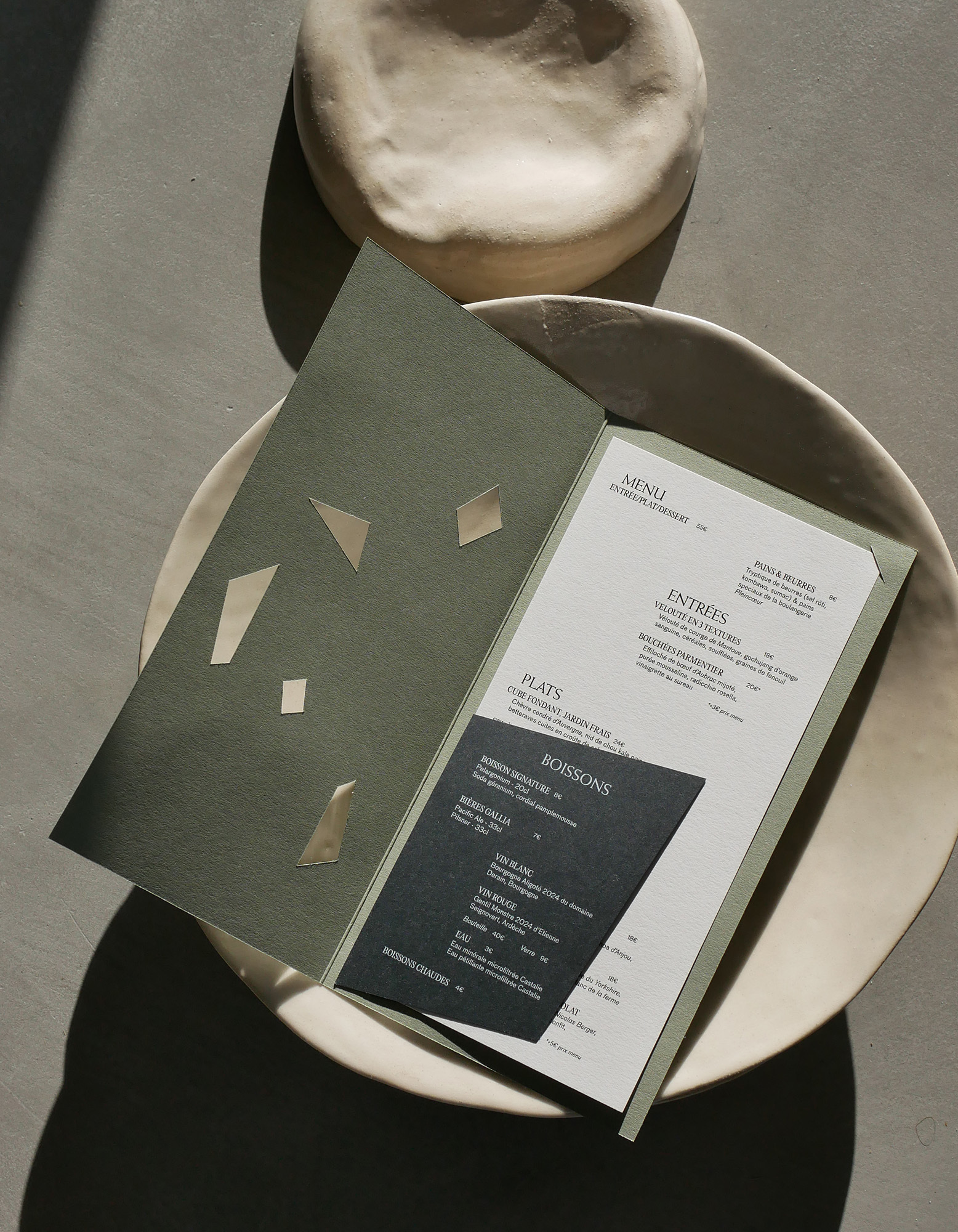 An open green restaurant menu resting inside a large ceramic bowl on a concrete surface with dramatic lighting