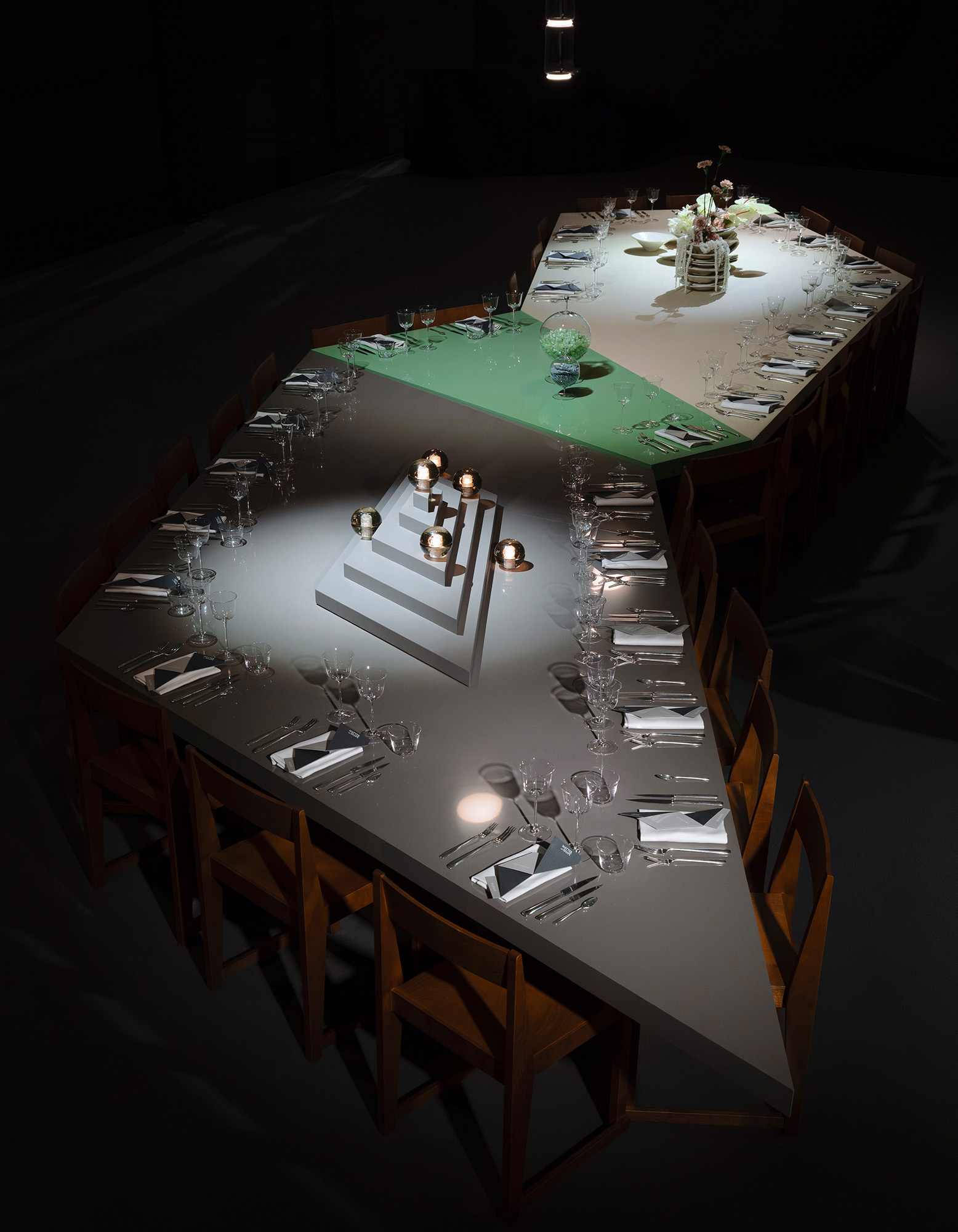 High-angle shot of a long geometric dining table featuring segmented color sections and dramatic spotlighting in a dark room