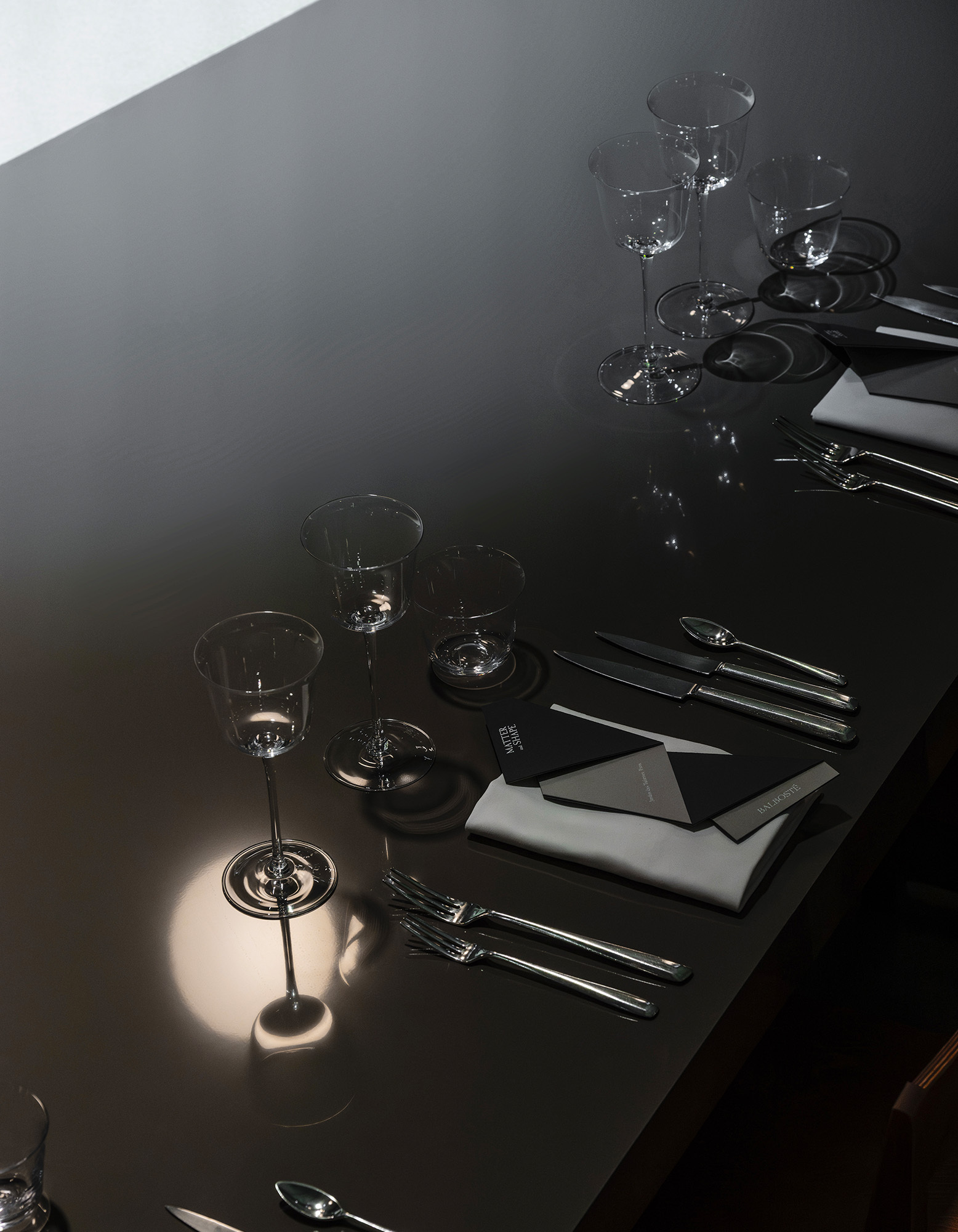 High angle shot of a sleek dark tabletop set with glassware, cutlery, folded napkins, and stationery for Matter and Shape.