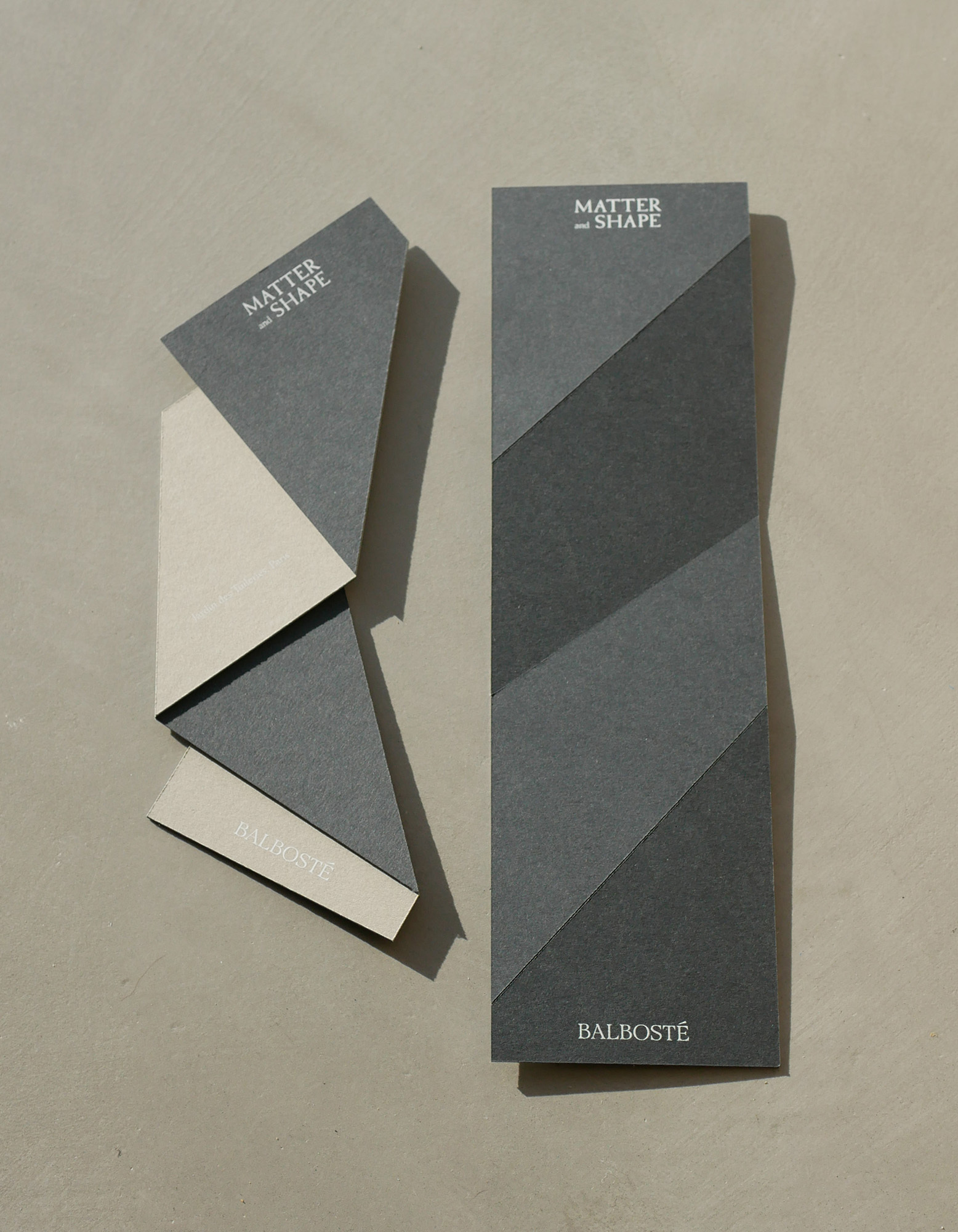 Minimalist geometric printed paper collateral and packaging design pieces arranged on a smooth neutral concrete surface