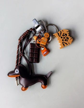 Leather dachshund keychain charm attached to metal rings with chocolate bar, gingerbread man, and orange letter charms.