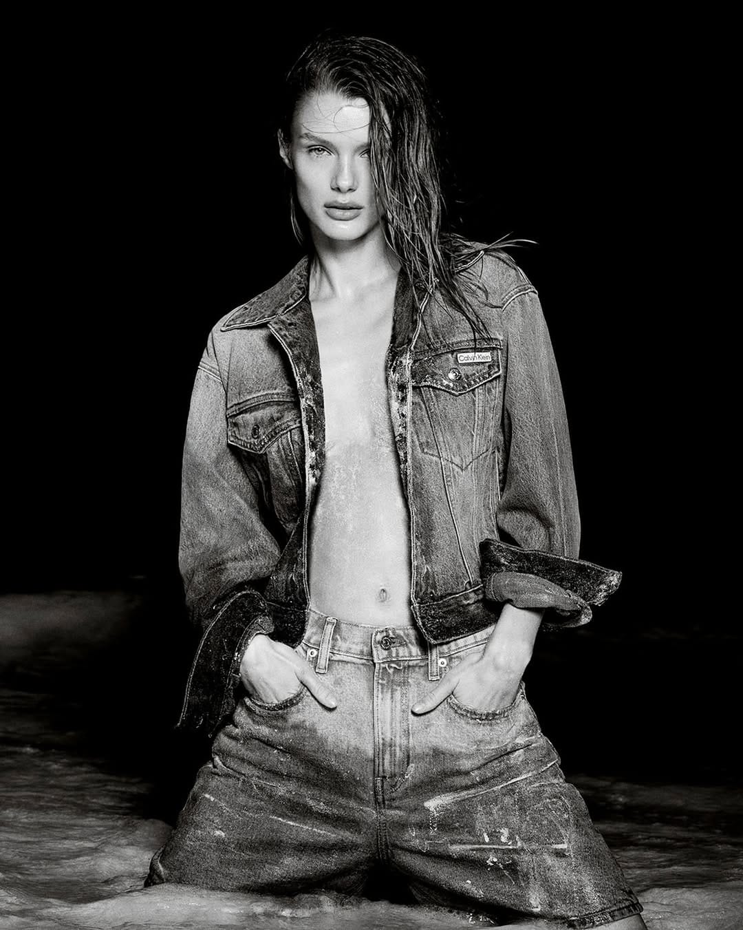 Model with wet hair wearing denim jacket and jeans posing in water for Calvin Klein Summer 2025 ad campaign.