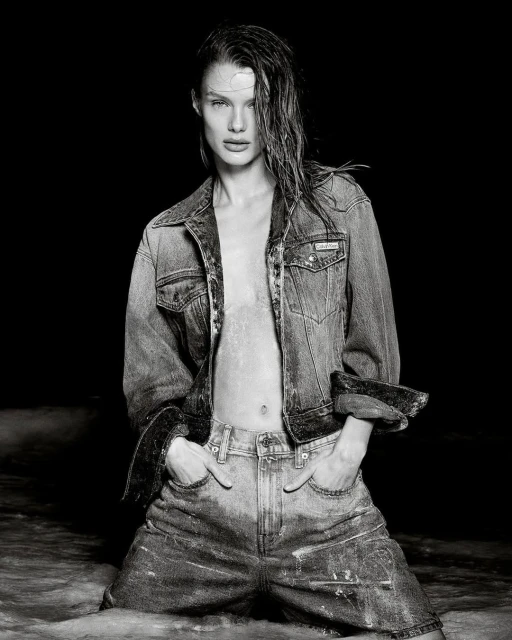 Model with wet hair wearing denim jacket and jeans posing in water for Calvin Klein Summer 2025 ad campaign.