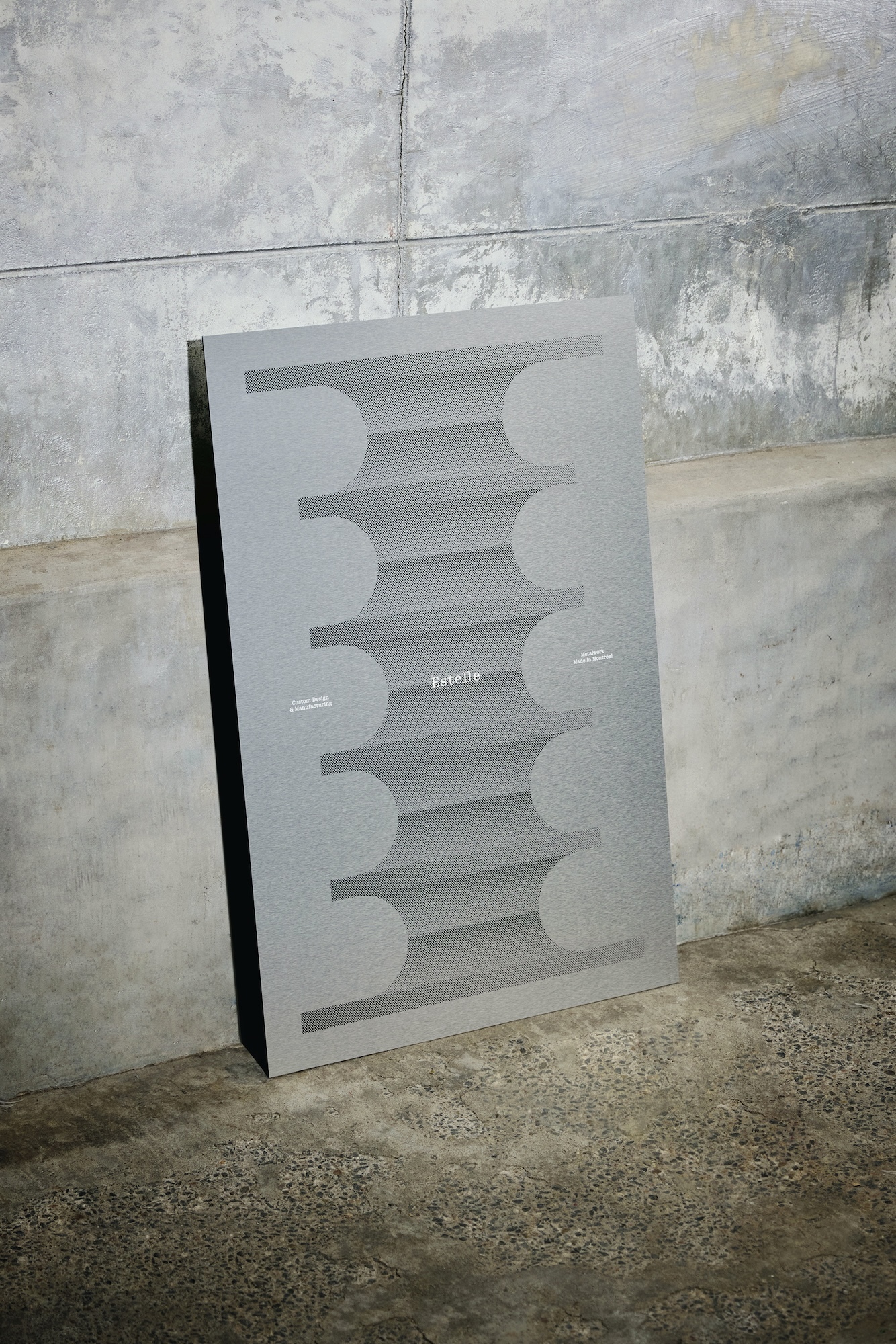 A grey vertical poster featuring a symmetrical geometric pattern leaning against a weathered concrete wall