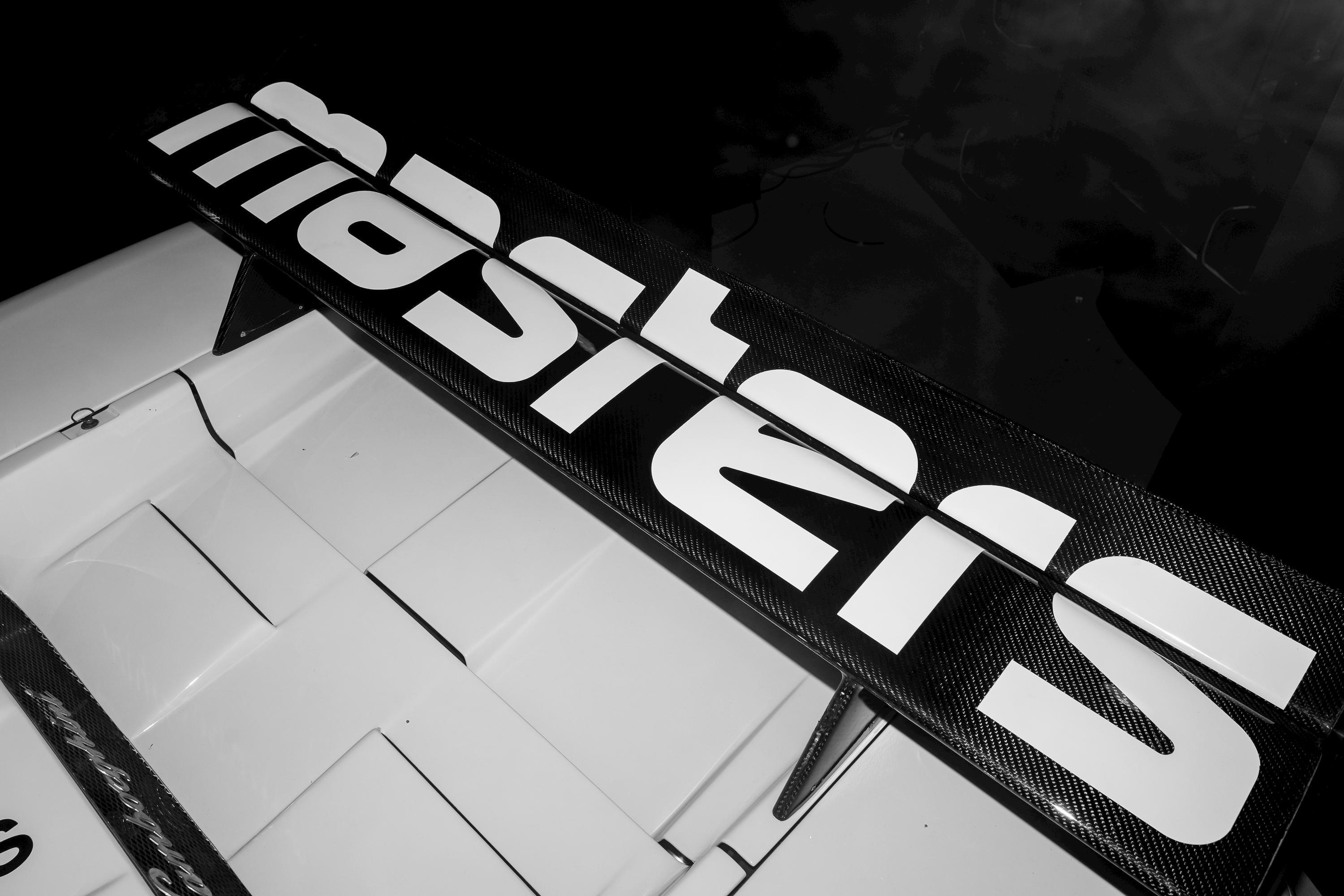 Close-up black and white shot of a racing car rear wing featuring the bold Masters Historic Racing logo in white.