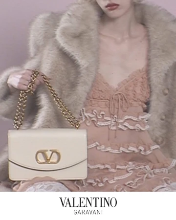 Model holding a cream leather handbag with gold chain strap wearing a textured faux fur coat and ruffled pink dress