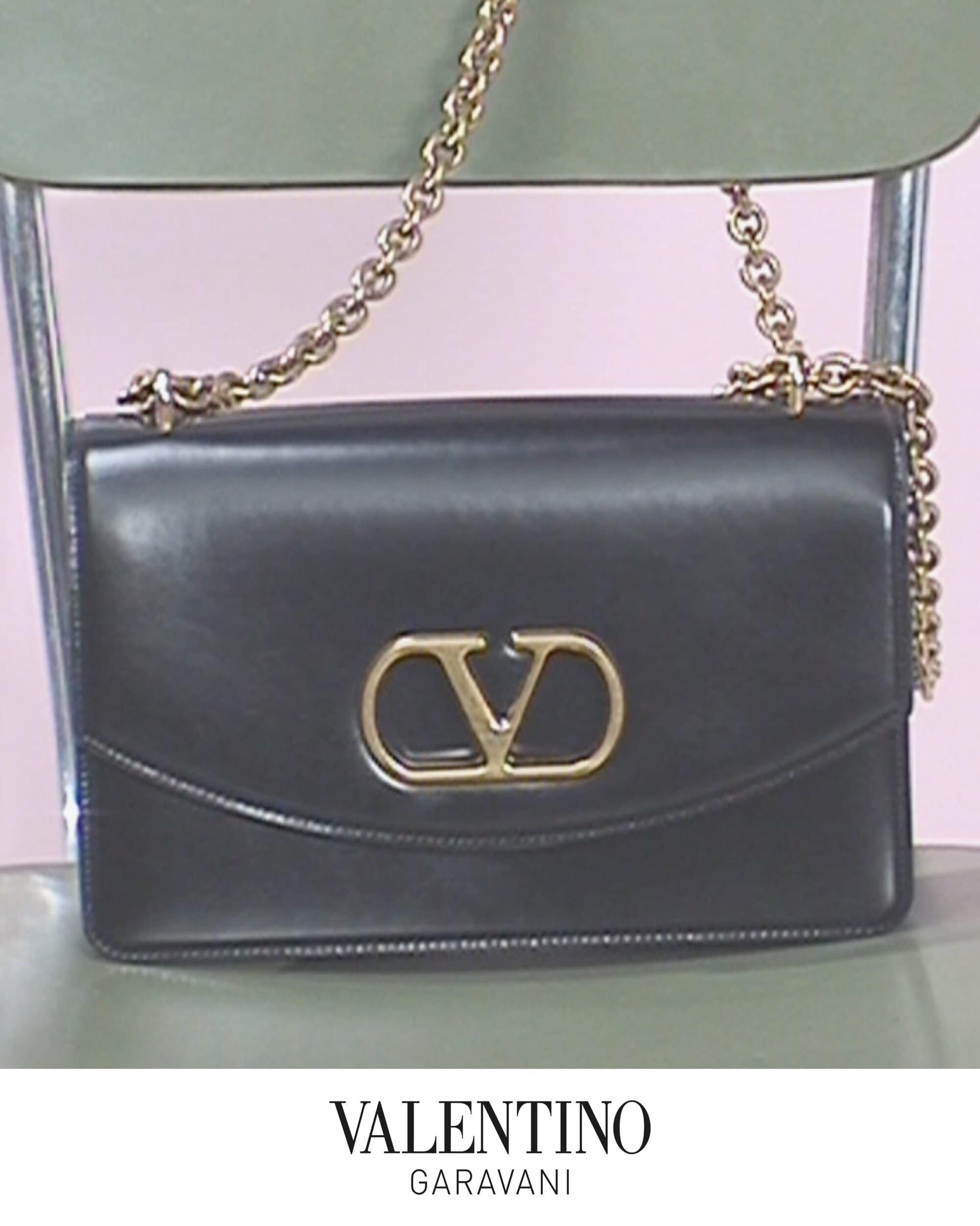 Black leather shoulder bag with gold chain strap and metal V logo resting on a green chair