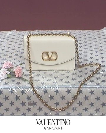 Valentino Garavani Vain bag with gold chain strap on a star-patterned surface beside pink flowers