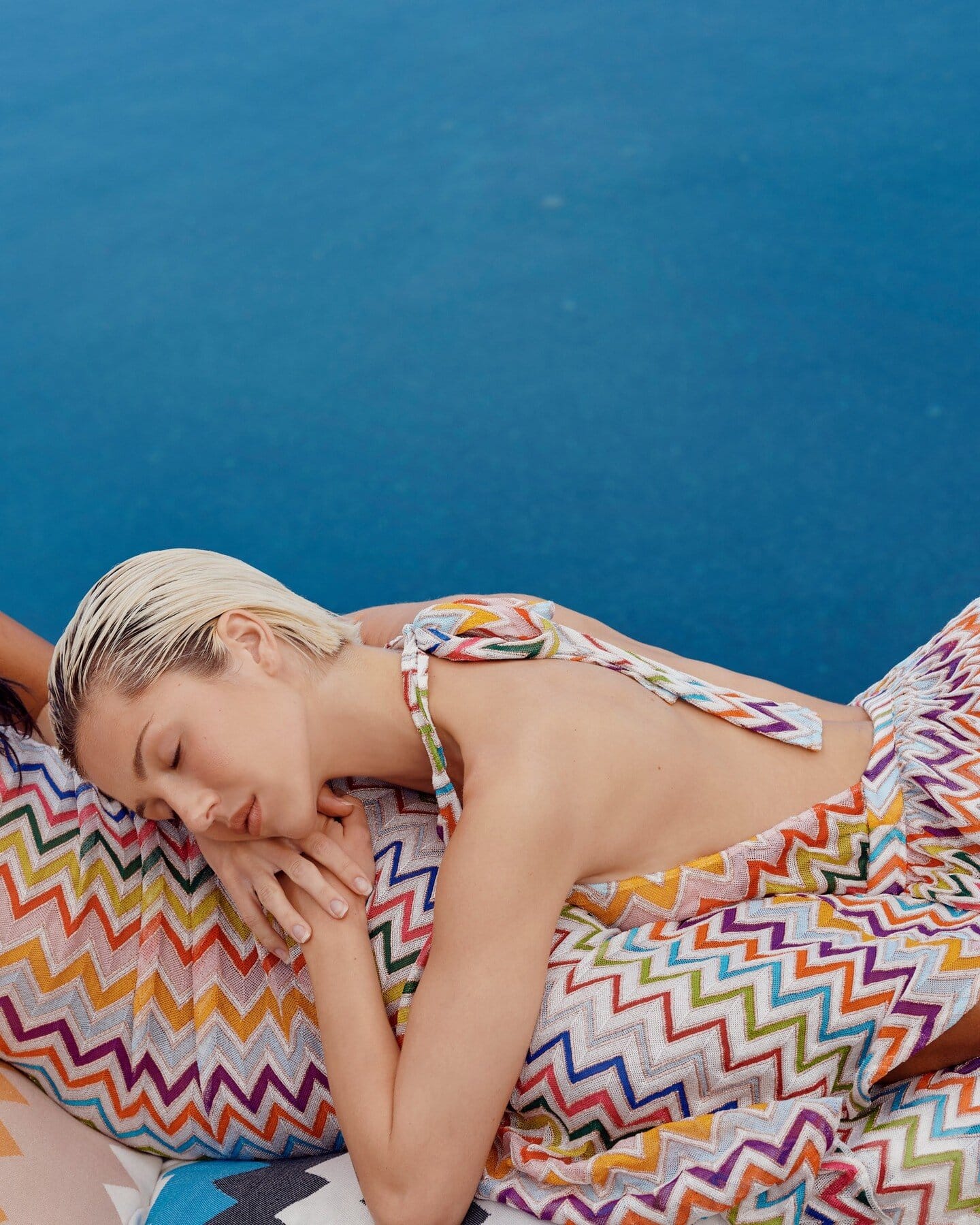 Two models wearing patterned multicoloured chevron outfits resting against a blue background