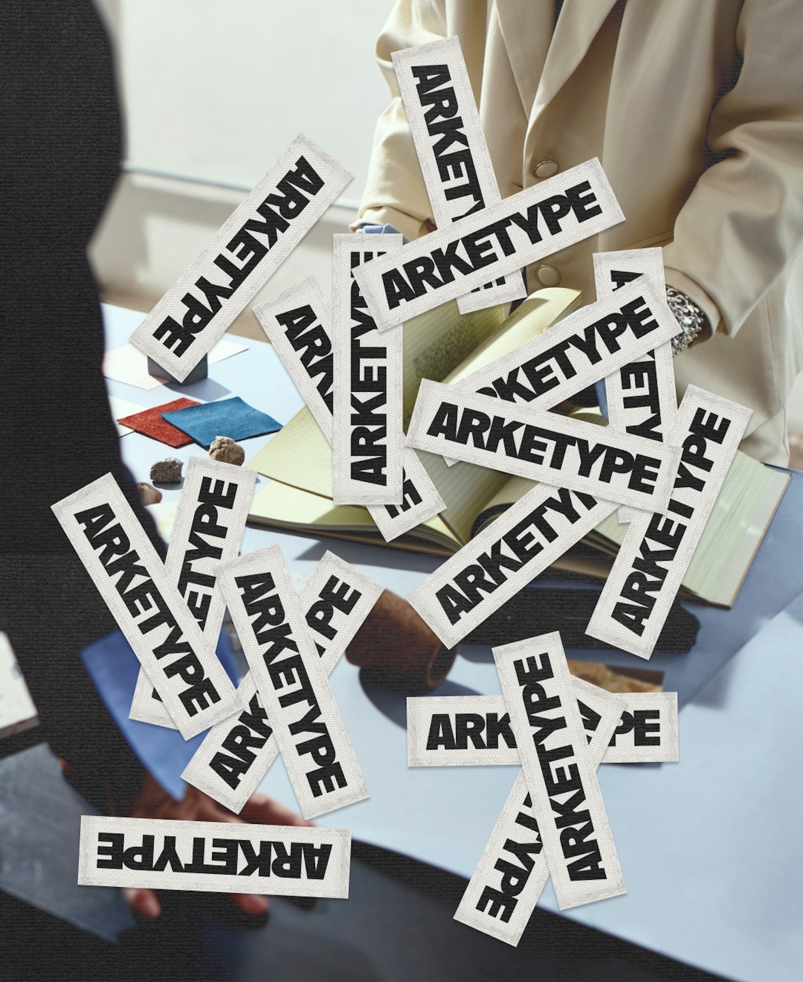 Falling label tags featuring ARKETYPE branding over an open book and desk surface