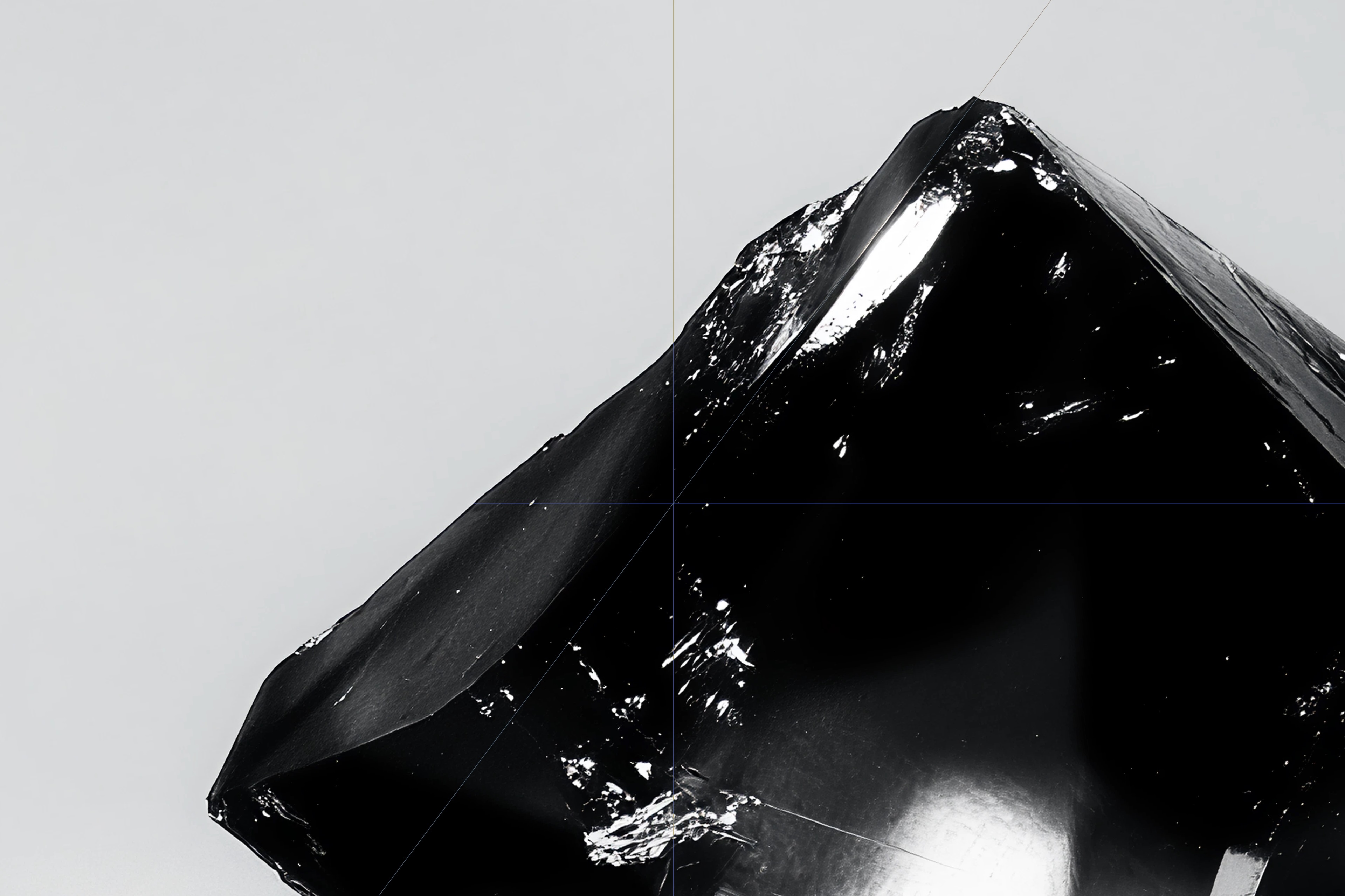 Close-up of a glossy black geometric object with sharp edges against a plain light grey background.