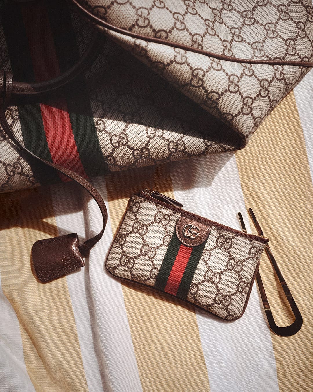 Gucci monogram canvas bags featuring signature red and green web stripes displayed on a striped fabric background