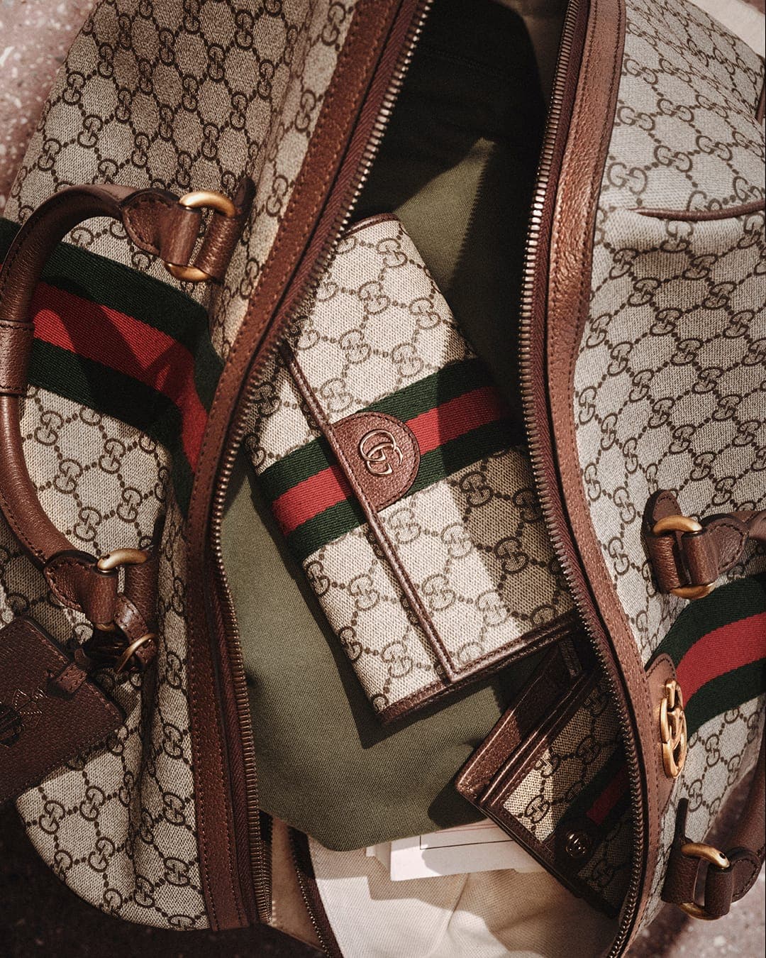 Close-up overhead view of an open Gucci monogram duffel bag filled with accessories and a wallet.