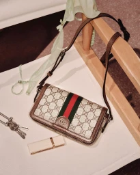 Gucci monogram shoulder bag resting on a white surface alongside keys, lipstick, and a green scarf draped over a wooden chair.