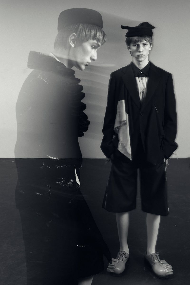 Monochrome fashion shot of a young adult man in an oversized suit and hat, with double exposure effect creating a ghostly second figure.