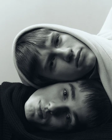 Monochromatic portrait of two young people, one wearing a hooded garment, close together in a fine art portrait style.