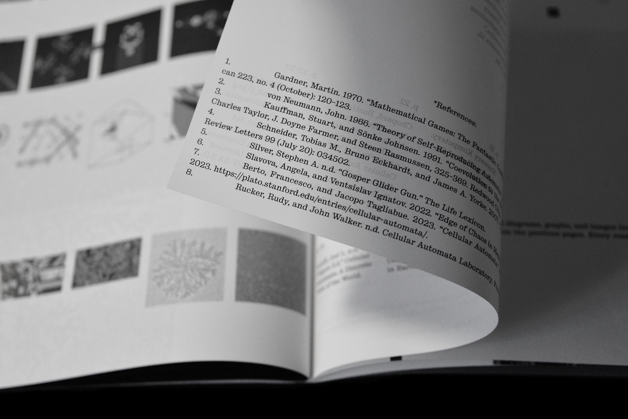 Close-up monochrome view of a curved book page with printed text and reference lists, set against a background of small diagrams.