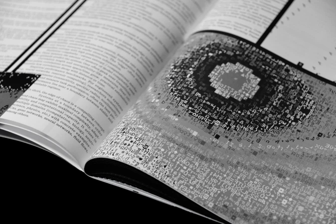 An open book displaying black and white printed text and a complex digital code pattern graphic across the pages.