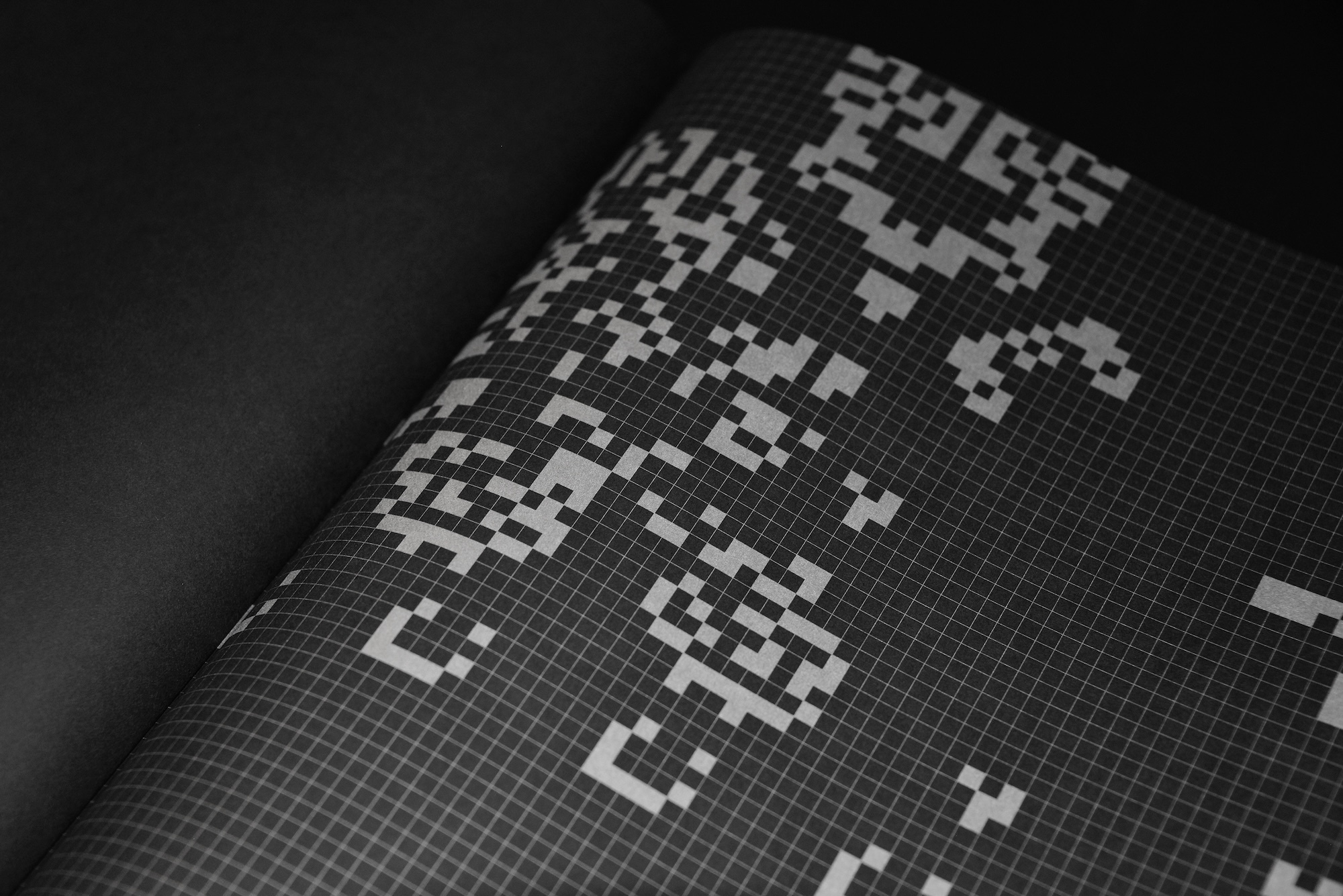 Close-up macro shot of a printed grid paper page with pixelated black and white graphic patterns.