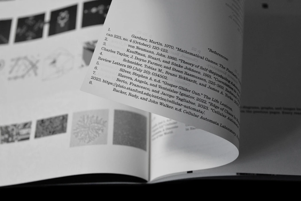 Close-up monochrome view of a curved book page with printed text and reference lists, set against a background of small diagrams.