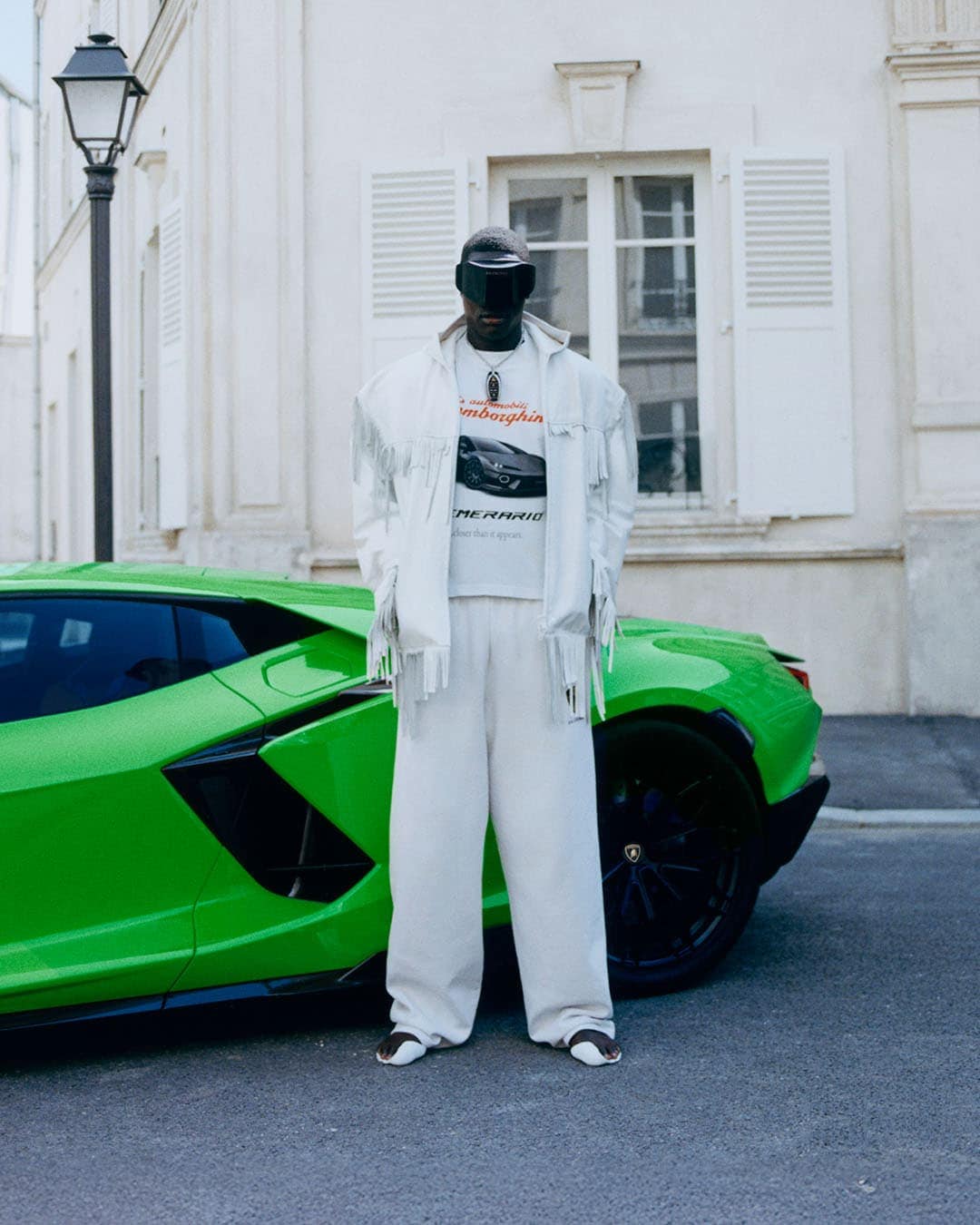 Model wearing a white fringed jacket and visor standing next to a bright green sports car on a street