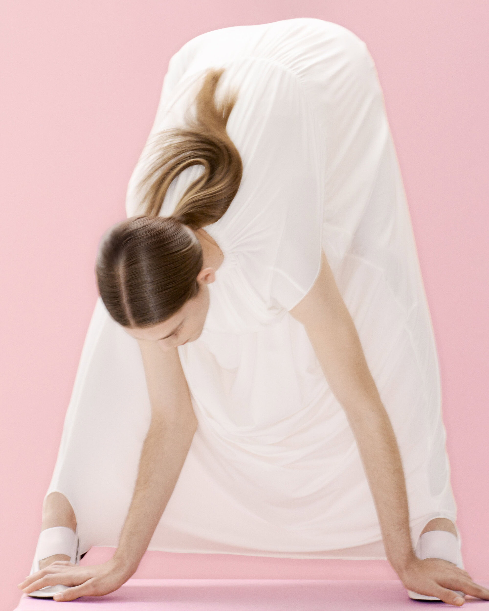 Model wearing a white dress bending forward on a pink seamless backdrop photographed by Marili Andre for Alainpaul.
