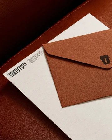 Brown textured envelope and branded letterhead resting on a dark red leather surface.