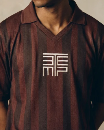 Close-up of a person wearing a brown and black striped polo shirt with an embroidered white logo on the chest.