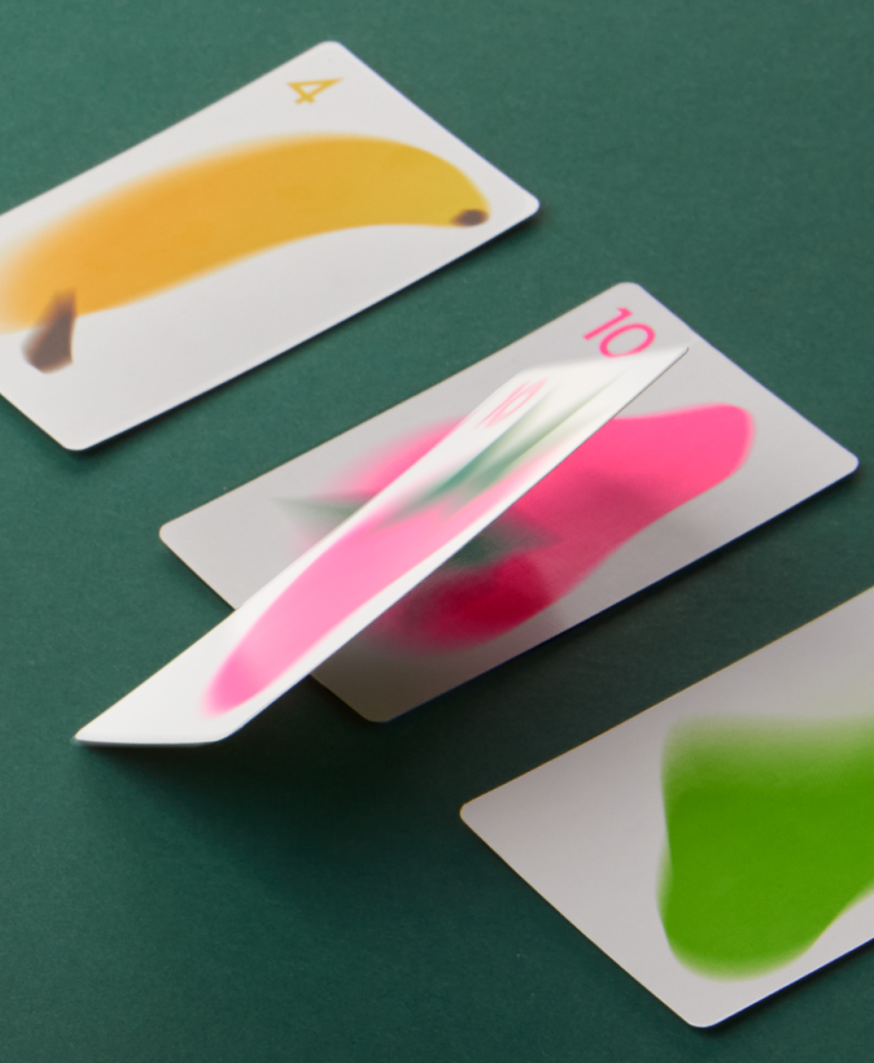 Playing cards with colourful fruit illustrations displayed on a dark green felt surface.