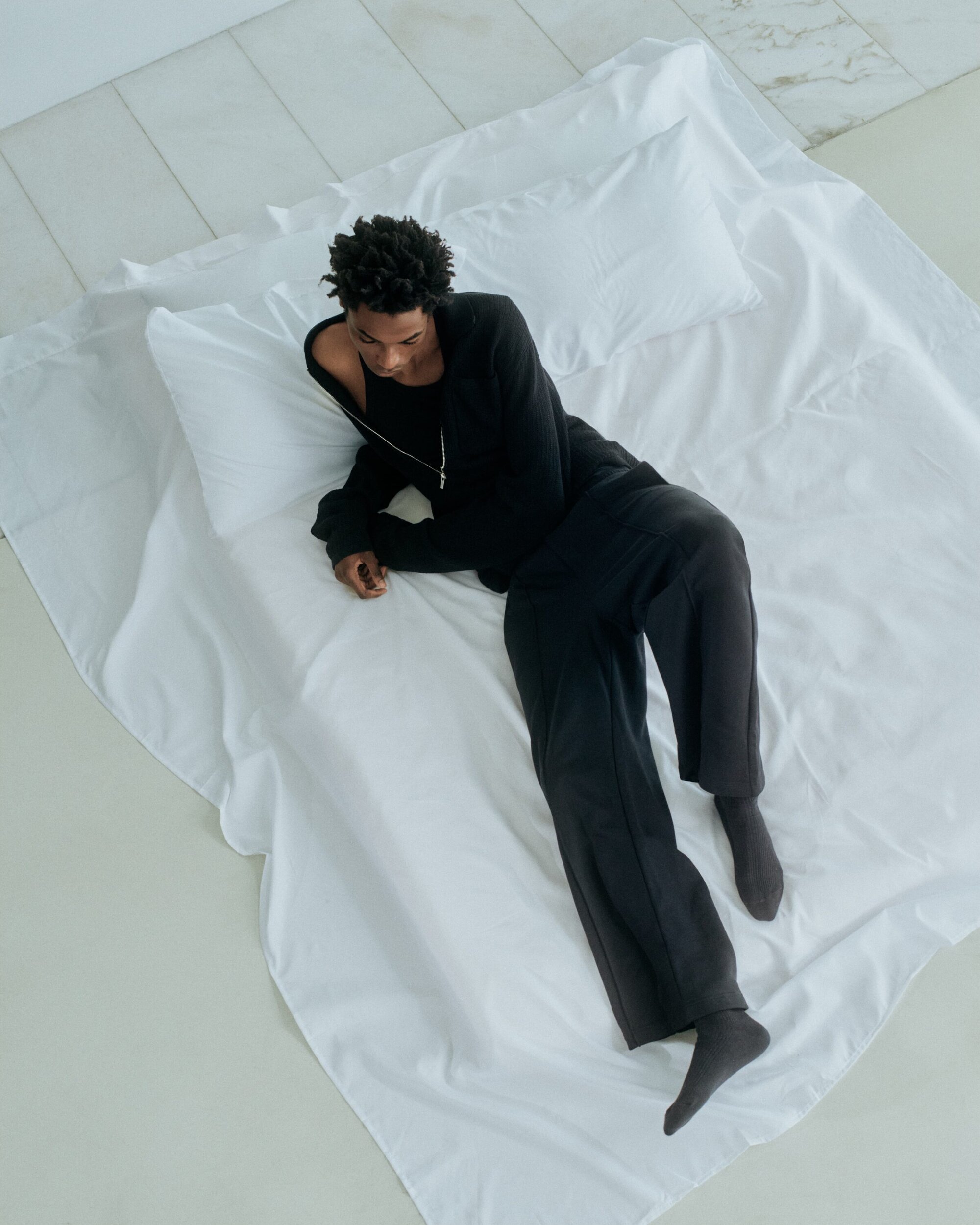 Model lying on white sheets in black clothing viewed from above for Helmut Lang