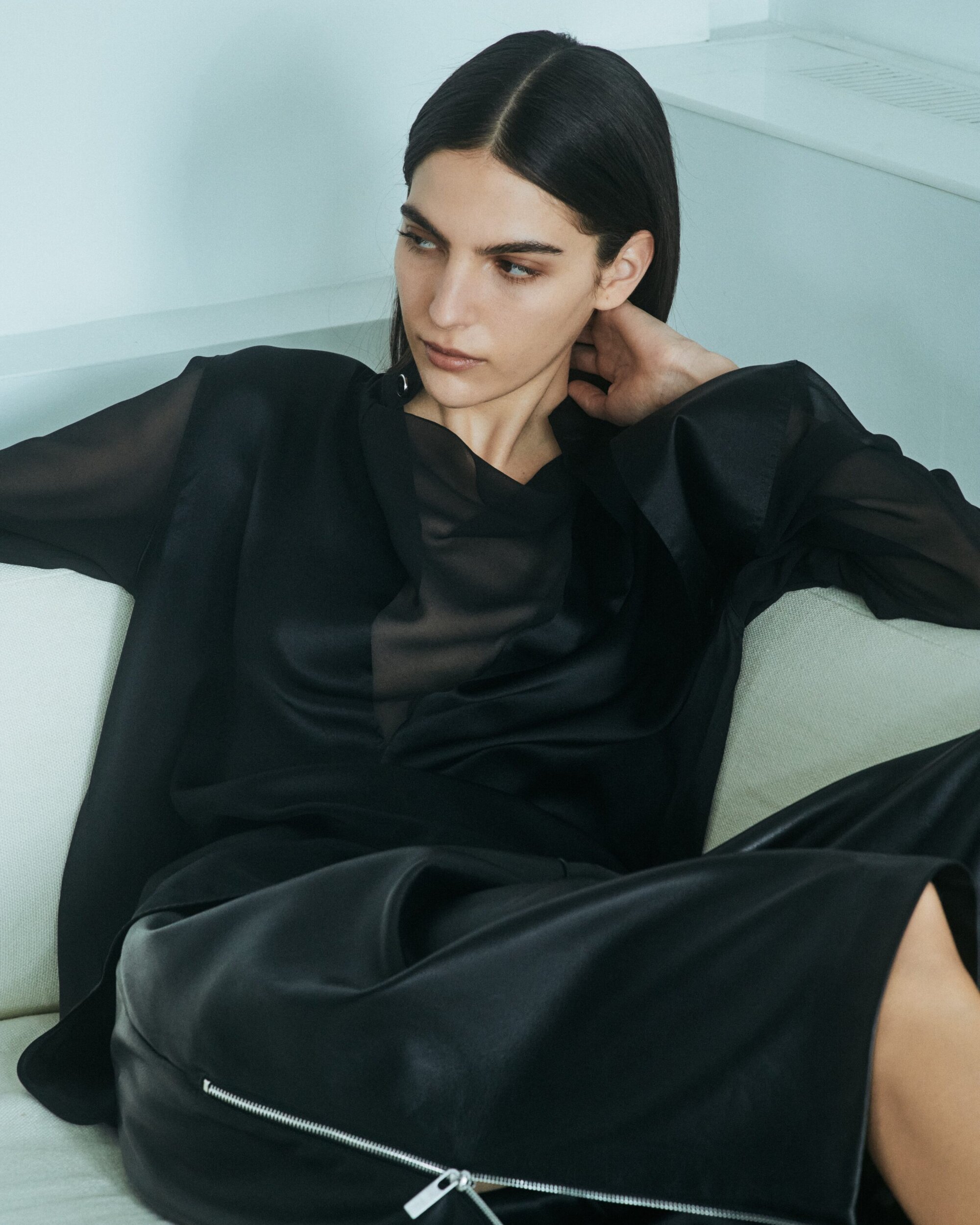 Model wearing a black top and dark trousers seated on a white sofa for the Helmut Lang pre-Fall 2024 ad campaign