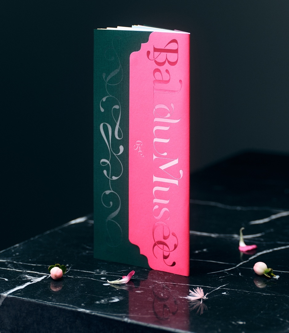 Vertical image of a pink and dark green folded program booklet standing upright on a dark marble surface.