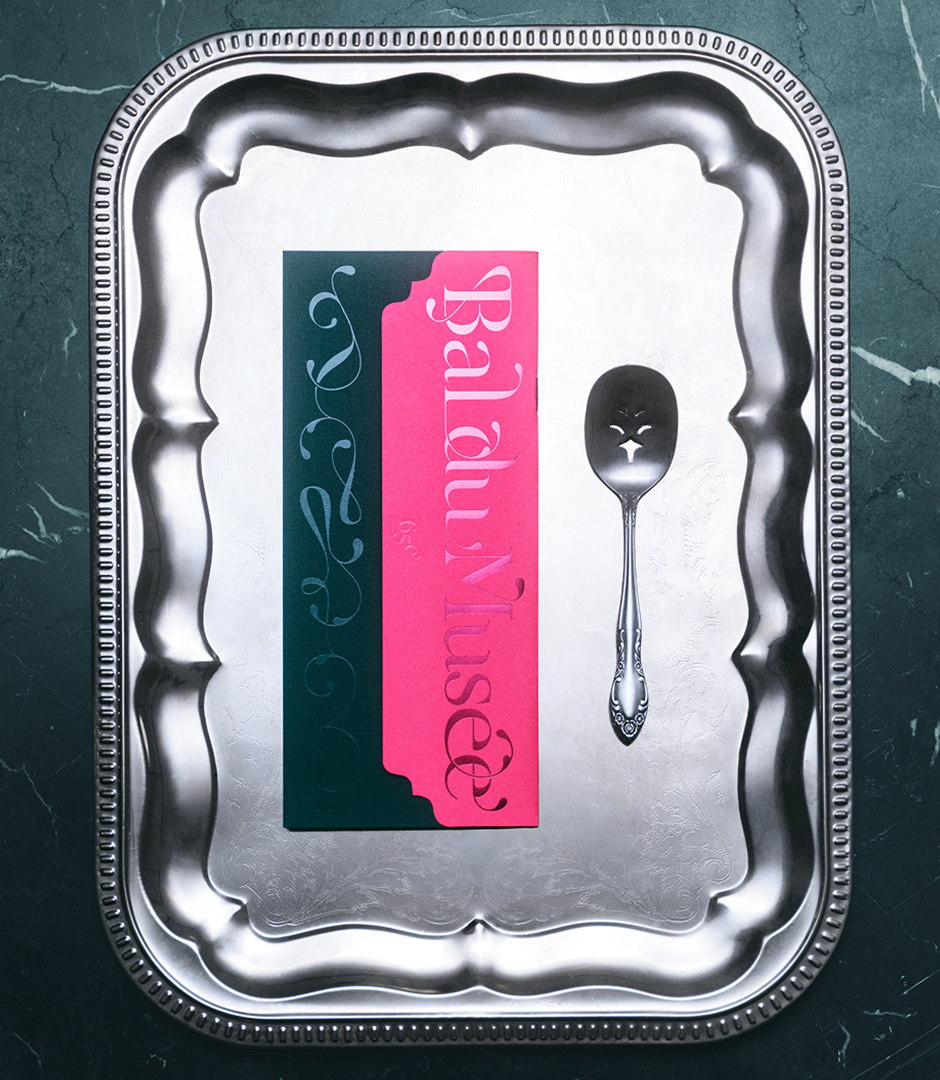Overhead view of a silver decorative tray featuring a pink and dark green card alongside a pierced silver spoon on a green marble surface.