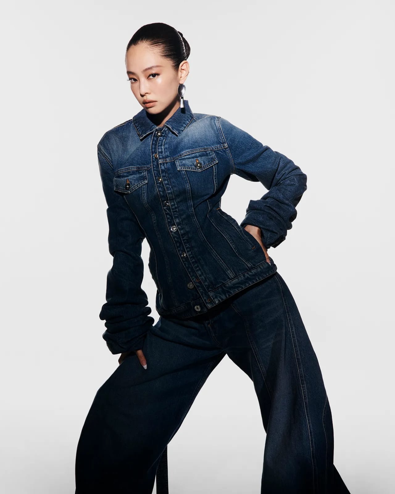 Jennie posing in a dark denim jacket and matching jeans against a plain white studio background for Jean Paul Gaultier.