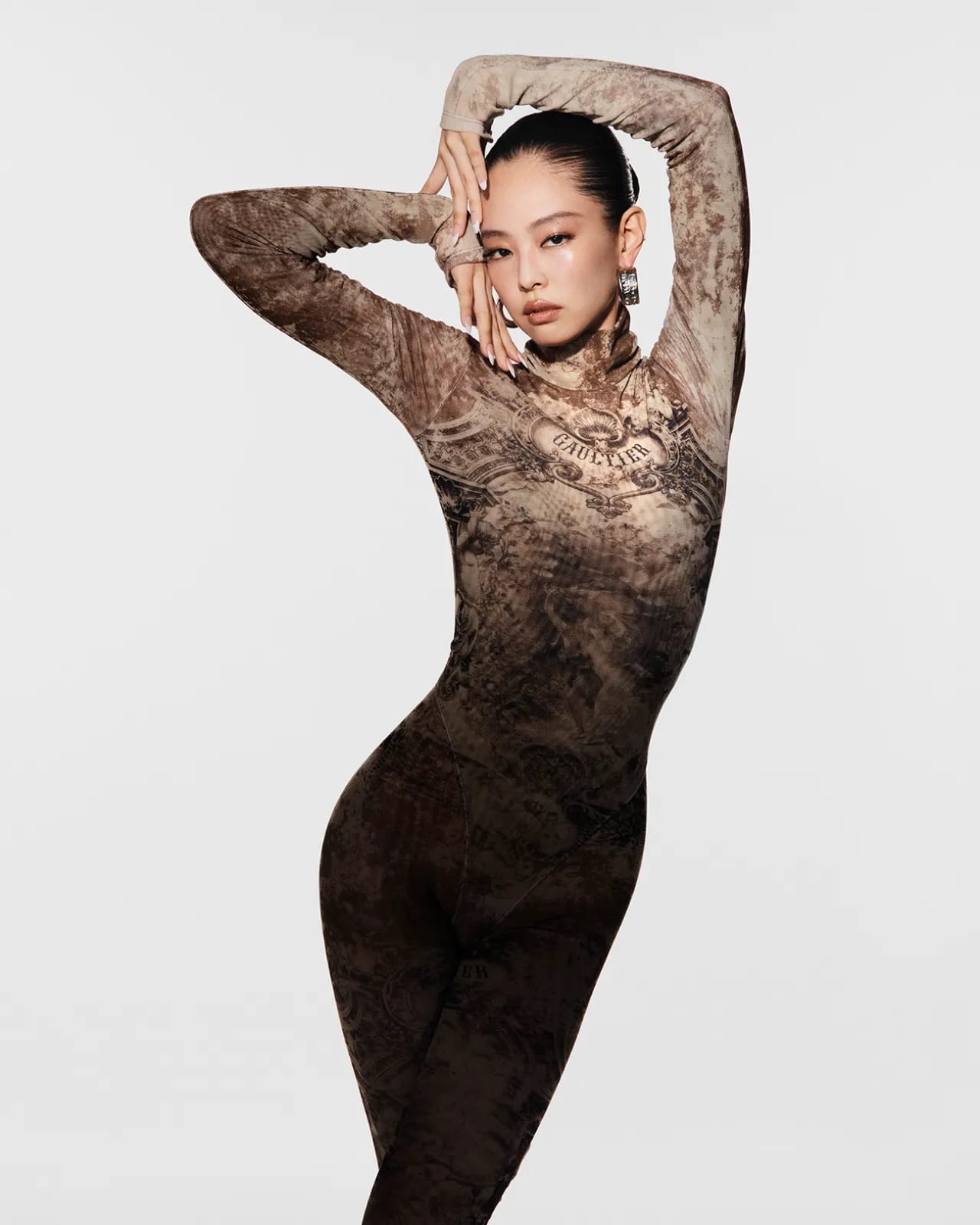 Jennie posing in a printed long-sleeve bodysuit with arms raised against a plain white studio backdrop