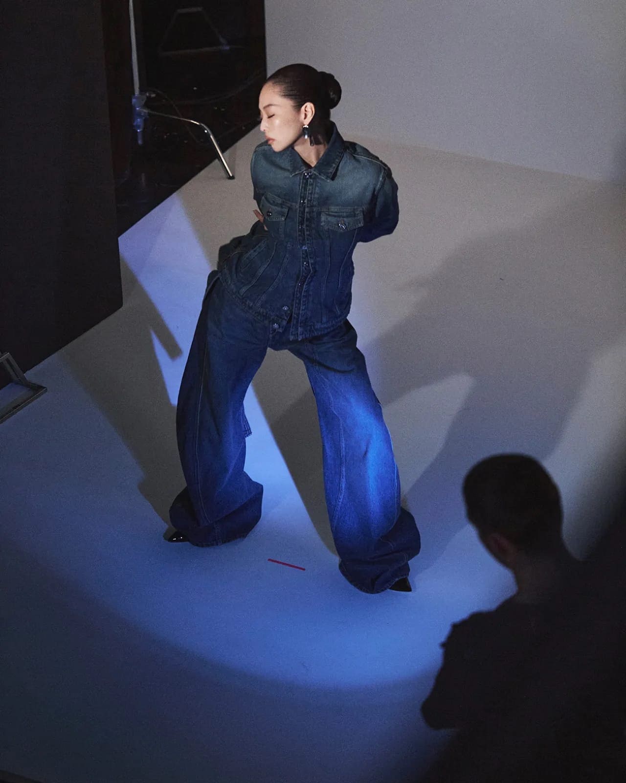 Model Jennie wearing a structured denim jacket and wide-leg trousers on a studio backdrop for Jean Paul Gaultier.