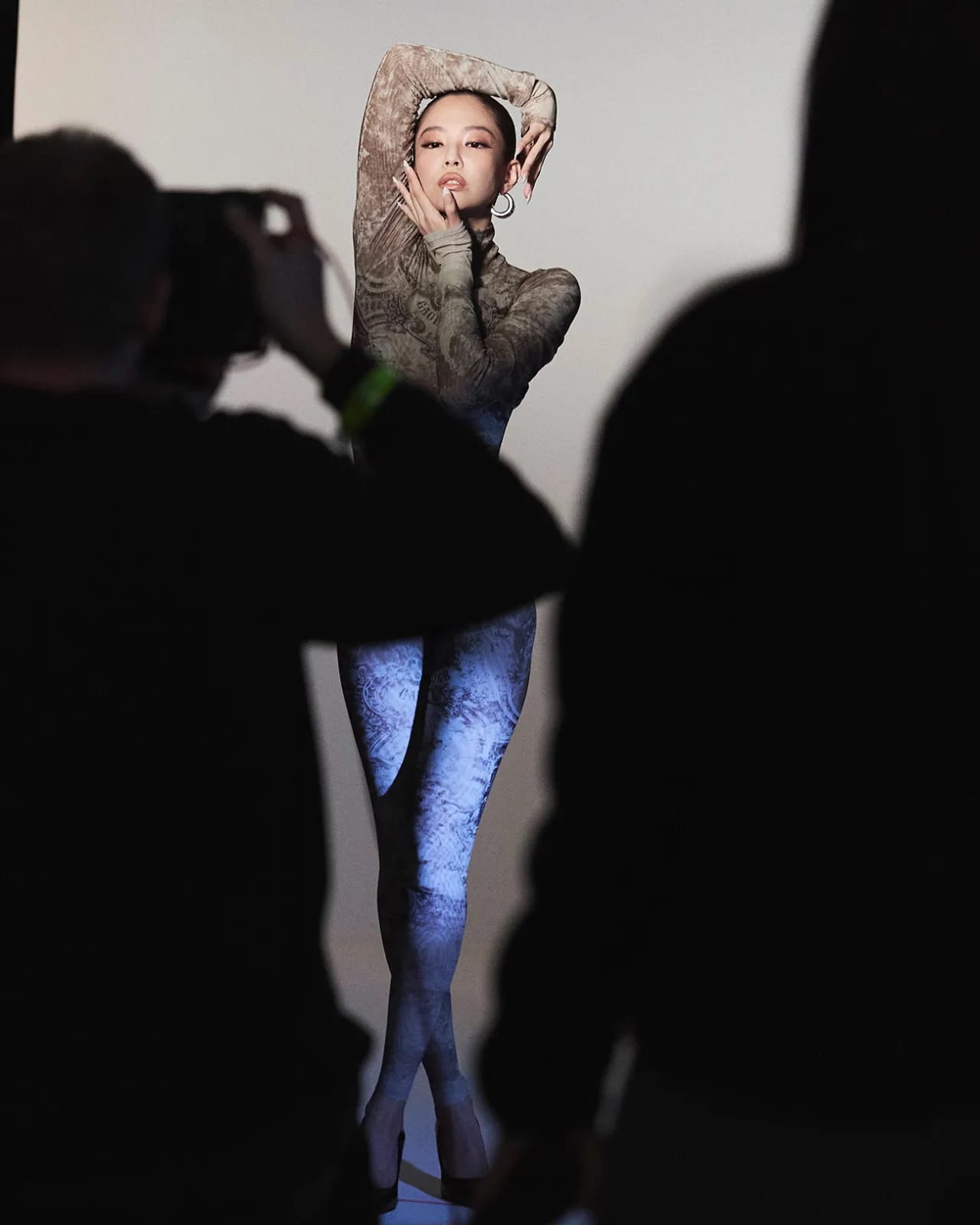 Model Jennie in patterned bodysuit posing in studio with crew silhouettes in foreground