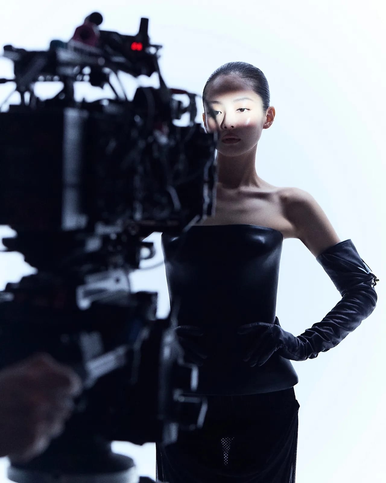 Model Jennie in black strapless top and long gloves on set behind a professional cinema camera for Jean Paul Gaultier ad campaign