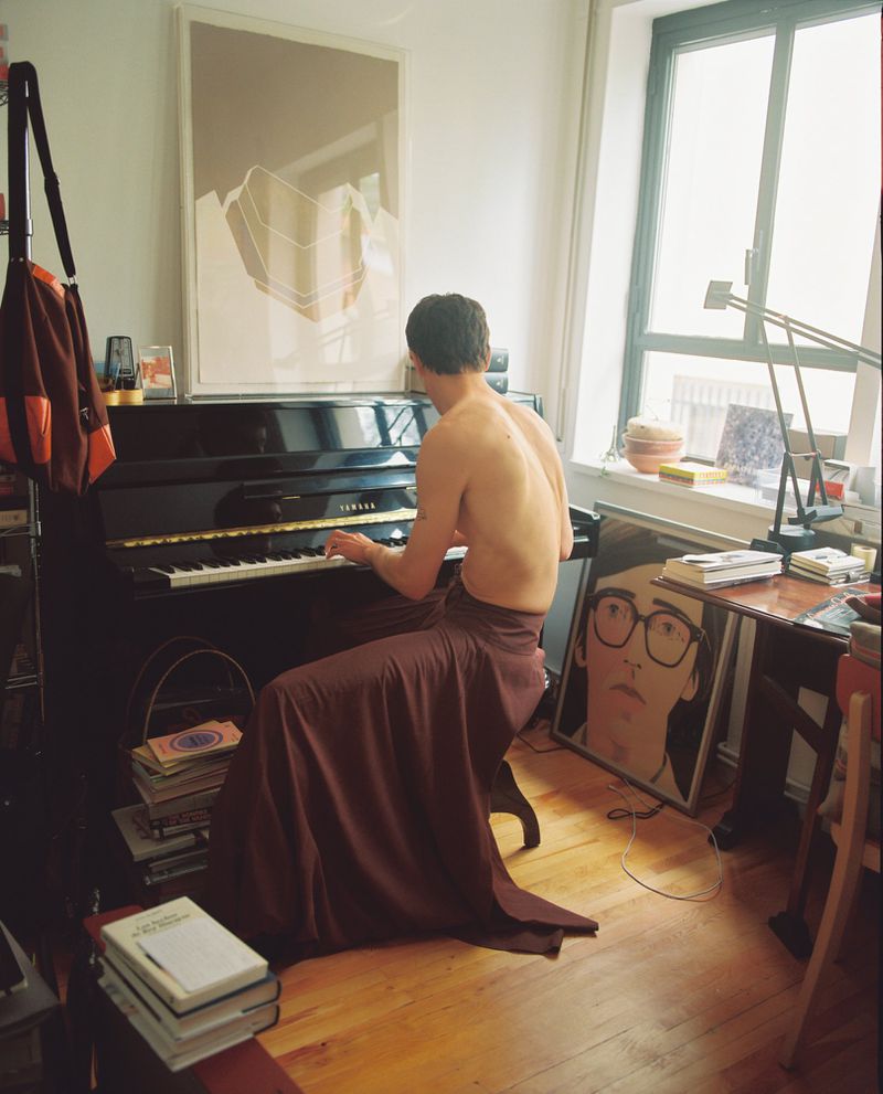 Back view of a person playing a black Yamaha piano in a room with natural light, books, and artwork for a creative, musical scene.