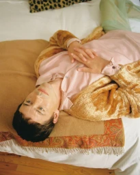 Model lying on a bed wearing a pink shirt and furry gold cardigan for El Pais Icon Magazine